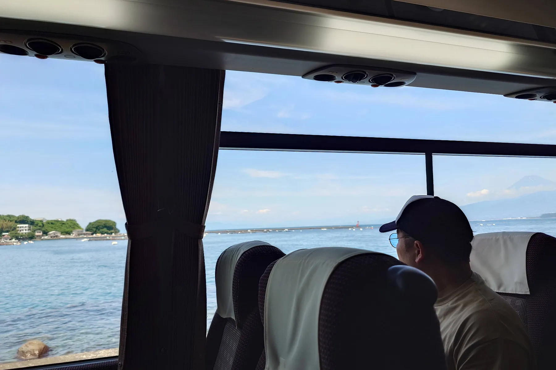 バスの車窓越しの海とそれを眺める人物